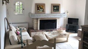 A cozy living room with a fireplace, a sofa, a chair, and a television. - Delightful provencal style villa on a single level with pool and stunning views. (Tourrettes)