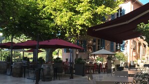 An outdoor café area with stone flooring, tables, and red umbrellas. - Delightful provencal style villa on a single level with pool and stunning views. (Tourrettes)