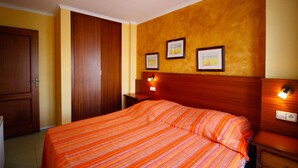 A hotel room with a wooden headboard, a bed with a striped bedspread, two bedside tables with lamps, and framed pictures on the wall. - Apartment with stunning views, 2 bedroom in the port of Empuriabrava (Empuriabrava)