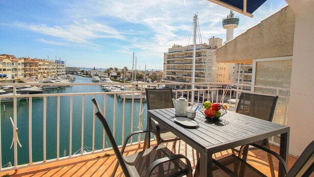 A balcony with a table, chairs, and a view of a marina with boats and buildings. - Apartment with stunning views, 2 bedroom in the port of Empuriabrava (Empuriabrava)