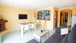 A modern living room with a dining area, a kitchen in the background, and a sofa with a remote control on it. - Apartment with stunning views, 2 bedroom in the port of Empuriabrava (Empuriabrava)