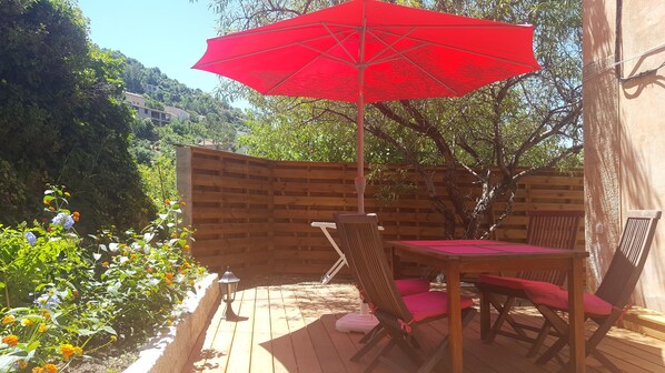 Une terrasse en bois avec une table et des chaises, un parasol rouge et une clôture en bois.
