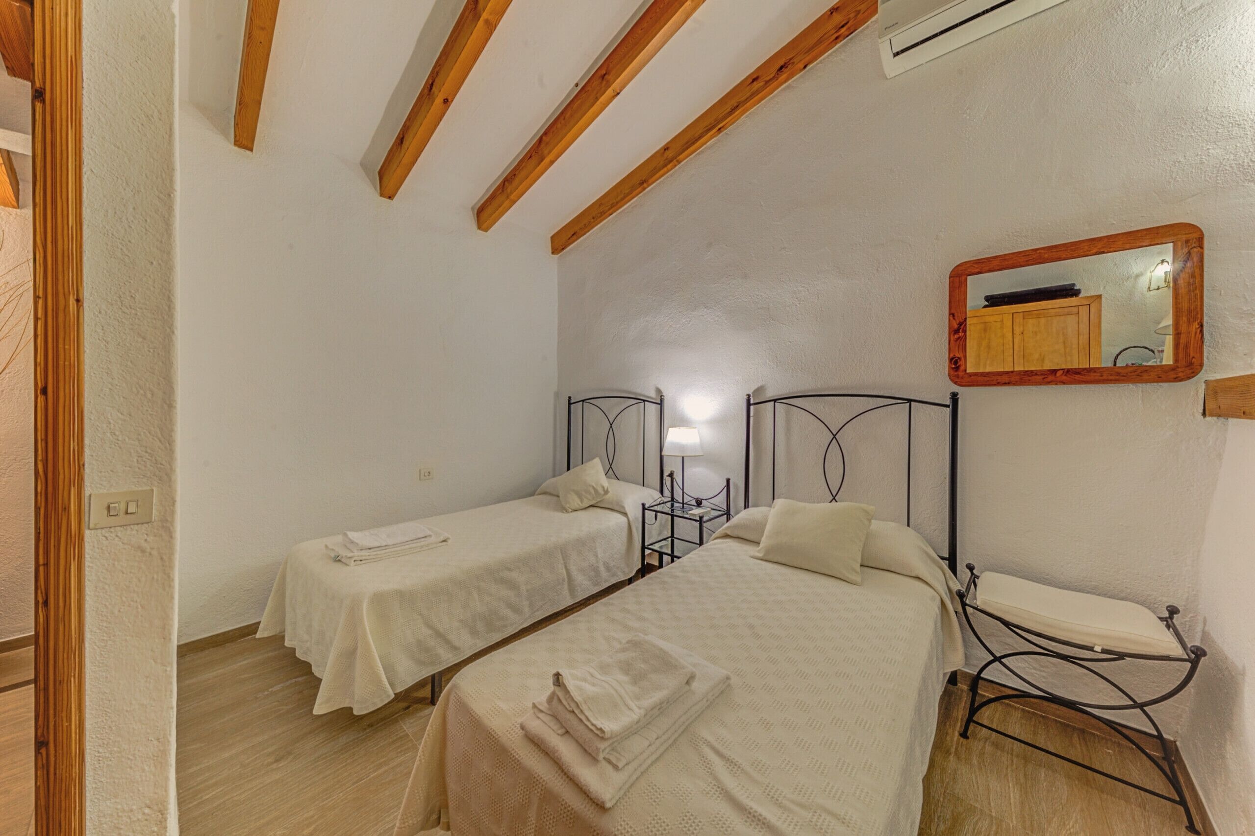 Ein Schlafzimmer mit zwei Einzelbetten, einem Nachttisch mit Lampe, einer Holzbalkendecke und einem Spiegel an der Wand.