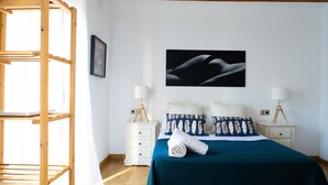 A bedroom with a bunk bed, a bed with a blue bedspread, two bedside lamps, and a framed artwork on the wall.