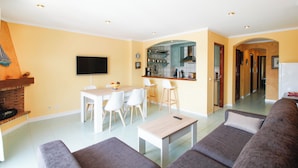 Una sala de estar moderna con un sofá, una mesita de centro y un televisor. Hay una zona de cocina con mostrador y taburetes.