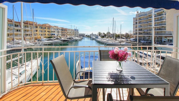 Un balcón con mesa y sillas, con vista a un puerto deportivo con barcos y edificios al fondo.