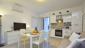 A modern kitchen with white cabinetry, a built-in oven, and a microwave. There is a dining area with a glass table and white chairs. - House in front of the beach of Balestrate (Balestrate)