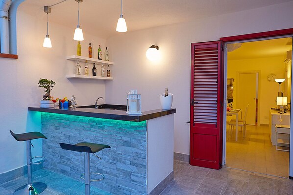 A modern kitchen with a bar area, a red door, and a dining area visible through an open door.