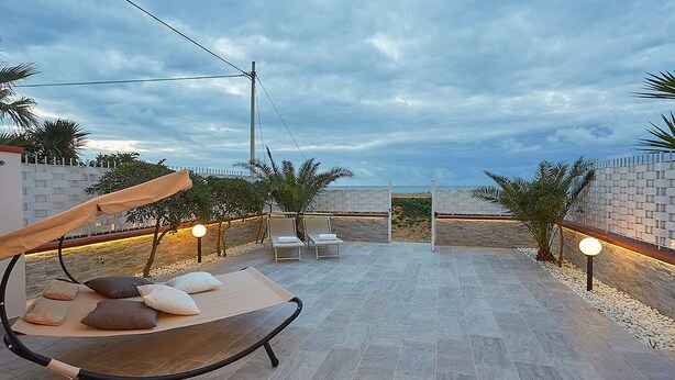 An outdoor patio with a swing chair, lounge chairs, and a view of the beach. - House in front of the beach of Balestrate (Balestrate)