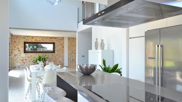 A modern kitchen with stainless steel appliances, a dining area with white furniture, and a stone wall with a window. - Son Sastre 024 luxurious villa with large swimming pool, air conditioning, garden and terrace (Muro)