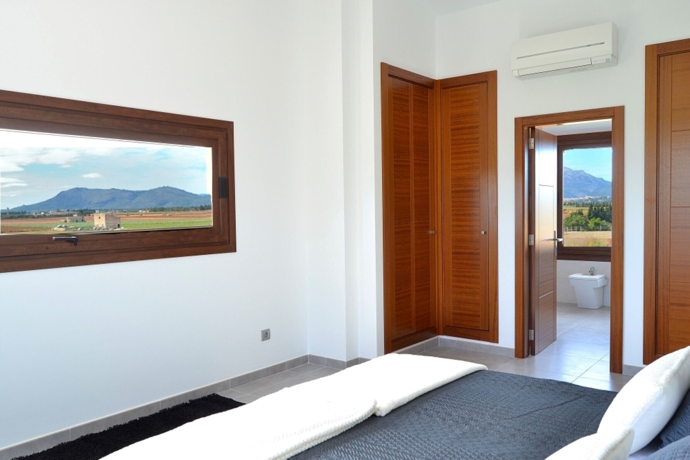 Un dormitorio con un ventanal amplio, un armario de madera y vistas a un paisaje montañoso.