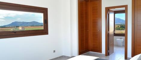 Un dormitorio con un ventanal amplio, un armario de madera y vistas a un paisaje montañoso.