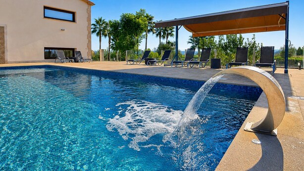 Una piscina con fuente, sillas de descanso y una zona de estar cubierta.