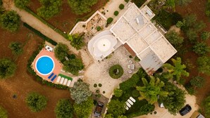 An aerial view of a property with a swimming pool, a tennis court, and a large building with multiple rooms.