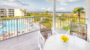 Un balcón con vista a la piscina, una mesa con un florero y una vista despejada de la playa y el océano.