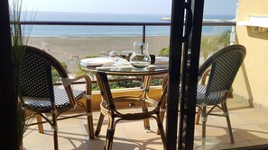 Un balcón con sillas de mimbre y una mesa de vidrio, con vista a la playa.