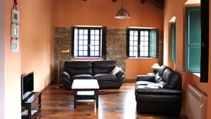 A cozy living room with a stone wall, two leather sofas, a wooden floor, and a television.