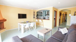 A living room with a sofa, a coffee table, and a TV. There's a kitchen area with a counter and chairs. - Bright apartment, 2nd floor, two rooms in the port of Empuriabrava (Empuriabrava)