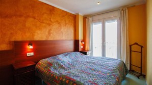 A hotel room with a large bed, wooden headboard, two bedside tables, a nightstand, and a window with curtains. - Bright apartment, 2nd floor, two rooms in the port of Empuriabrava (Empuriabrava)