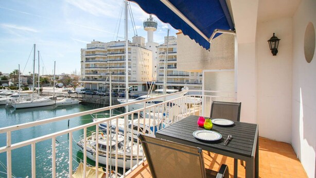 A balcony with a table set for two, overlooking a marina with boats and buildings in the background. - Bright apartment, 2nd floor, two rooms in the port of Empuriabrava (Empuriabrava)