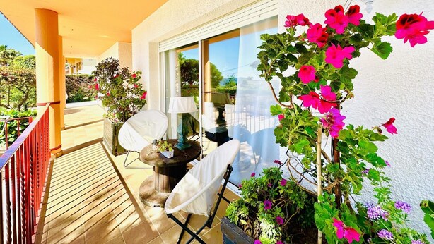 Ein Balkon mit weißer Brüstung, einem Tisch mit Stühlen und Topfpflanzen.
