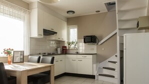 A modern kitchen with white cabinets, a dining table with chairs, a microwave, and a refrigerator.