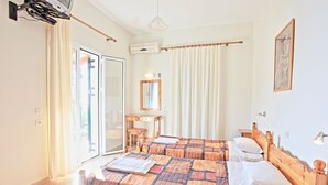Een hotelkamer met twee bedden, een bureau, een stoel, een spiegel en een groot raam met gordijnen.
