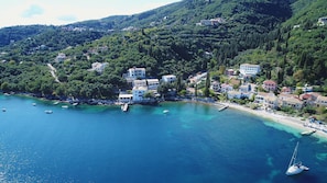 A coastal town with buildings along the shoreline, boats in the water, and a clear view of the surrounding hills.