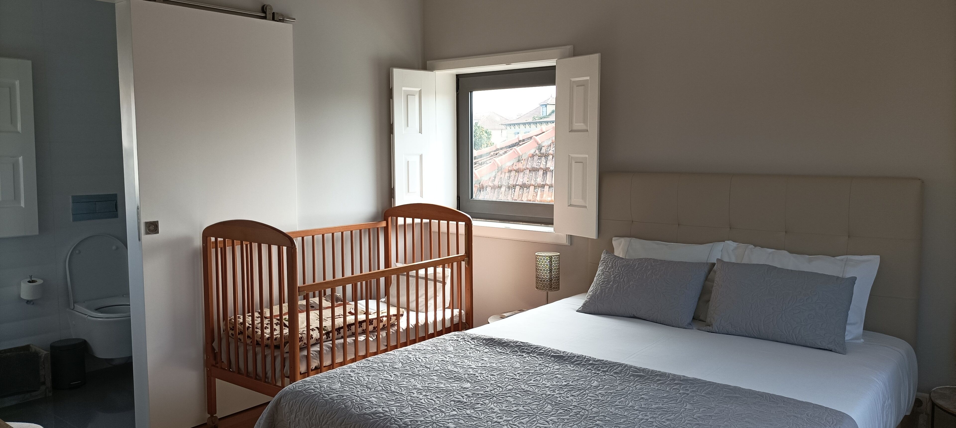 Ein Schlafzimmer mit einem Babybett, einem Bett mit Kissen, einem Fenster und einer Tür.