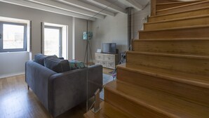 Ein modernes Wohnzimmer mit grauem Sofa, einer Holztreppe und einem Fernseher auf einem Schrank.