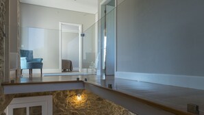 Ein modernes Interieur mit einer Steinwand, einer Holztreppe, einem grauen Sofa mit gemusterten Kissen und einer Glastür zu einem anderen Raum.