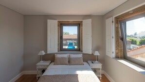 Ein Schlafzimmer mit einem großen Bett, zwei Nachttischen, einem Fenster mit Blick auf einen Pool und einer Tür mit geöffneten Fensterläden.