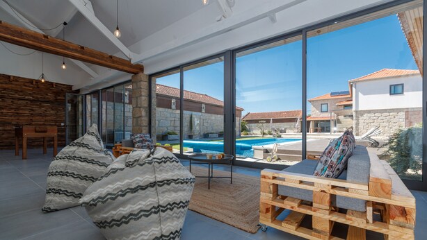 Ein modernes Wohnzimmer mit großen Fenstern, einem Pool und einer Couch aus Holzpaletten.