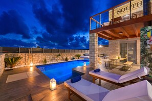 Un área de piscina en la azotea con pared de piedra, sillones de descanso y vista al cielo.