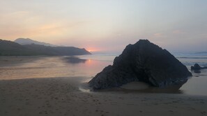 A beach with a prominent rock formation in the foreground and a sunset in the background. - Charming House in Ribadesella. Sea and Mountains for up to 4 people (Alea , Ribadesella)