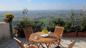 Une table en bois, entourée de quatre chaises, est placée sur une terrasse en pierre offrant une vue panoramique.