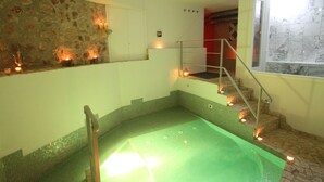 Un espace spa doté d’une piscine chauffée à l’eau verte, de murs en pierre et d’un escalier menant à un niveau supérieur.