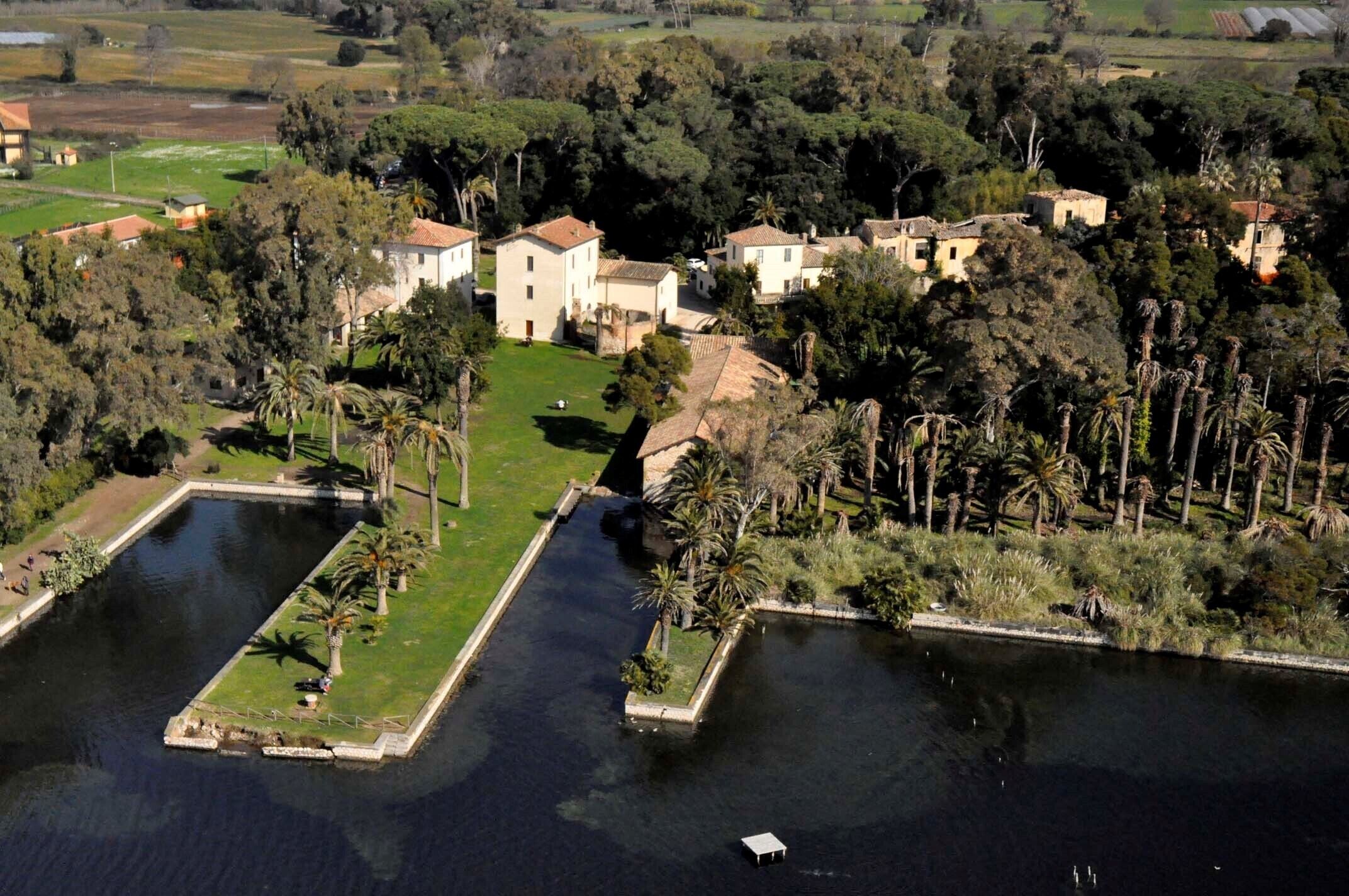 An aerial view of a property with multiple buildings, a large central structure, and surrounding greenery.