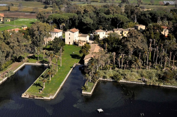 An aerial view of a property with multiple buildings, a large central structure, and surrounding greenery.