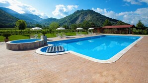 Une piscine entourée d’un patio en briques, agrémentée de chaises longues et de parasols, avec des montagnes en toile de fond.