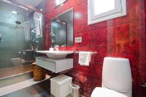 Moderni kylpyhuone, jossa on lasiseinällä varustettu suihku, valkoinen pesuallas ja wc.