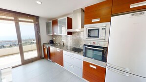 A modern kitchen with a built-in oven, microwave, and refrigerator, featuring wooden cabinets and a large window. - Apartment with Sea Views and Sunlit Terraces (Marbella)