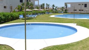 A pool area with two pools, surrounded by lounge chairs and umbrellas, with buildings in the background. - Apartment with Sea Views and Sunlit Terraces (Marbella)
