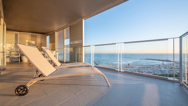 Ein Balkon mit zwei Liegestühlen, Blick auf das Meer und ein Parkplatz im Hintergrund.