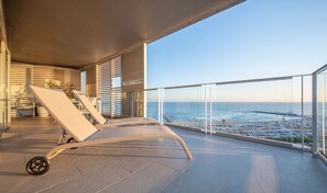 Un balcon avec deux chaises longues, une vue sur la mer et un parking en arrière-plan.