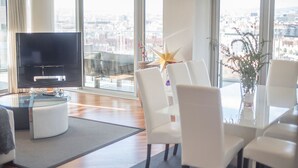 Ein modernes Wohnzimmer mit Flachbildfernseher, weißen Möbeln und großen Fenstern mit Blick auf die Stadt.