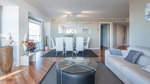 Ein modernes Wohnzimmer mit Glastisch, weißem Sofa und Essbereich mit Stühlen.