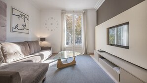 A modern living room with a sofa, a glass coffee table, a TV mounted on the wall, and a large window with curtains. - Three bedroom apartment Diagonal - You Stylish (Barcelona)