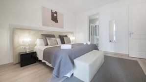 A modern bedroom with a large bed, bedside tables, a bench, and a door. - Three bedroom apartment Diagonal - You Stylish (Barcelona)