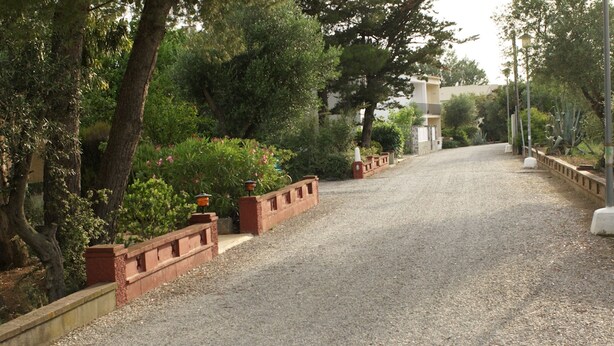 A gravel driveway leading to a building with a brick wall and greenery on the sides. - Sea view, terrace 20 m2, WIFI, parking, barbecue and garden of 1000 m2. (Roses, Girona)